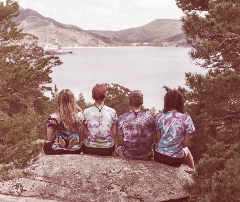 Four teen campers sigging on a rock overlooking a lake with mountains in the background